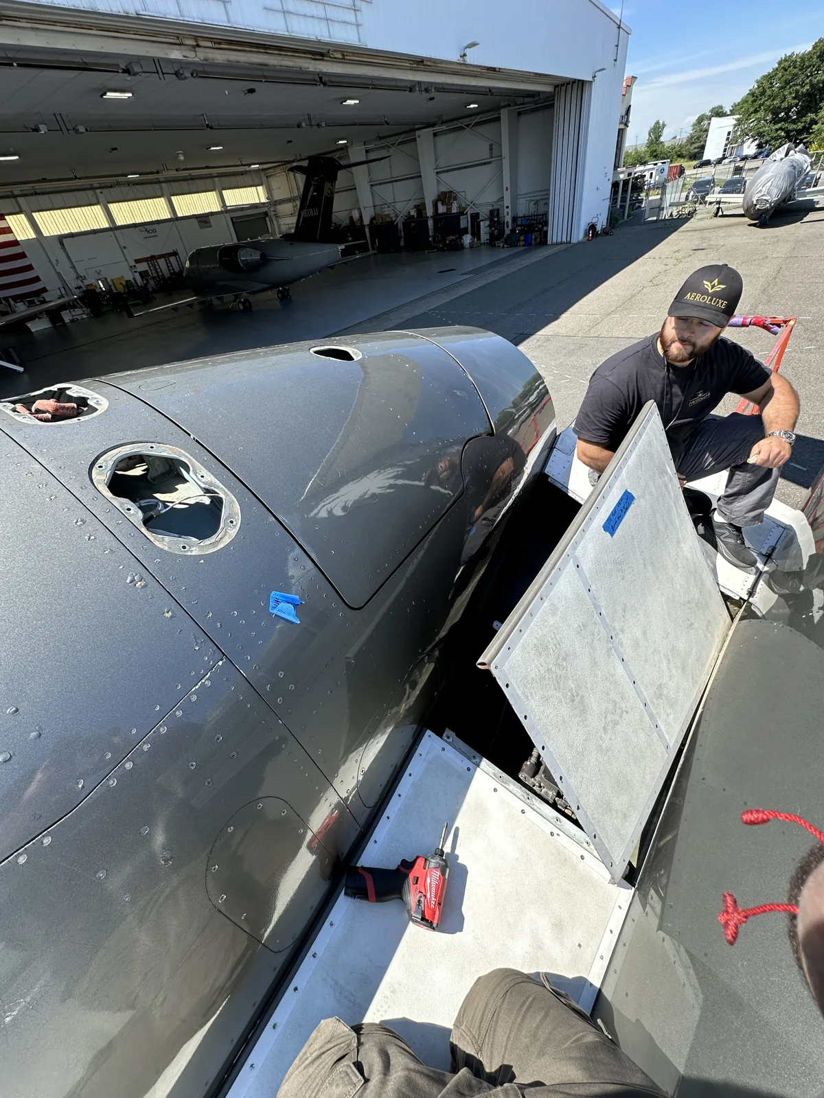 An Aeroluxe technician working at an open engine-access panel on a business jet.